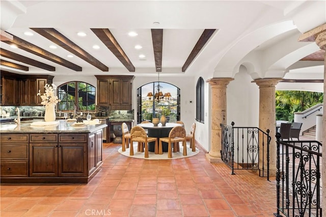 kitchen with hanging light fixtures, decorative backsplash, light stone countertops, and ornate columns