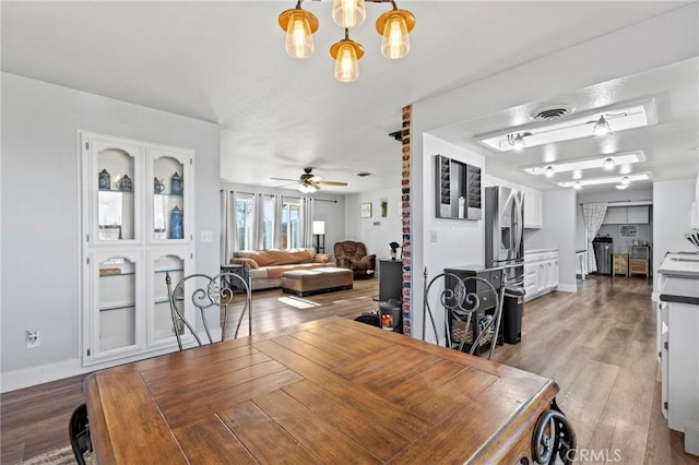 dining space with ceiling fan with notable chandelier and light hardwood / wood-style floors