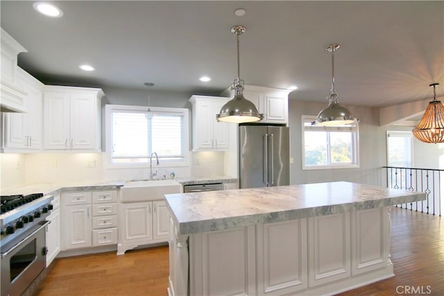 kitchen featuring premium appliances, a sink, decorative light fixtures, and white cabinetry