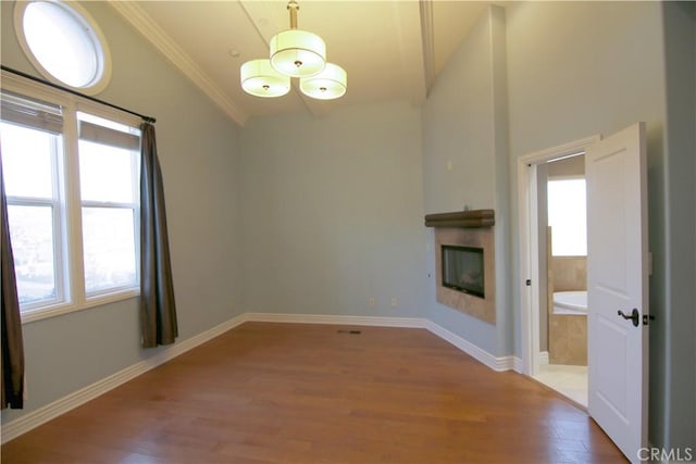 unfurnished living room with a wealth of natural light, a glass covered fireplace, crown molding, and light wood finished floors