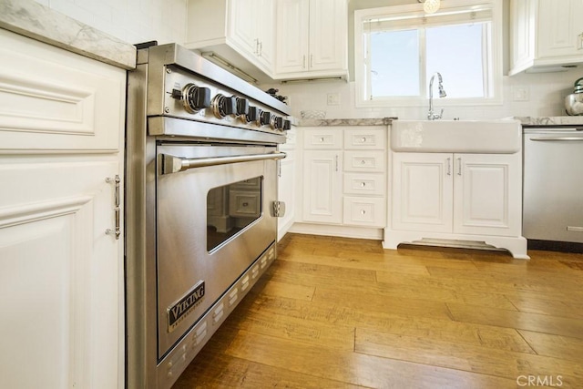 kitchen featuring designer stove, light countertops, stainless steel dishwasher, white cabinets, and a sink