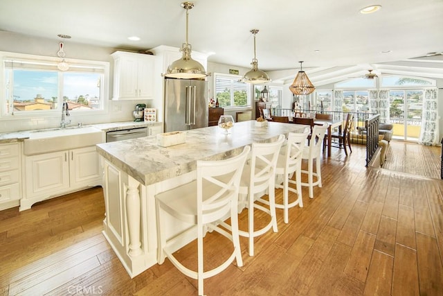 kitchen with stainless steel appliances, a sink, a center island, hanging light fixtures, and light stone countertops