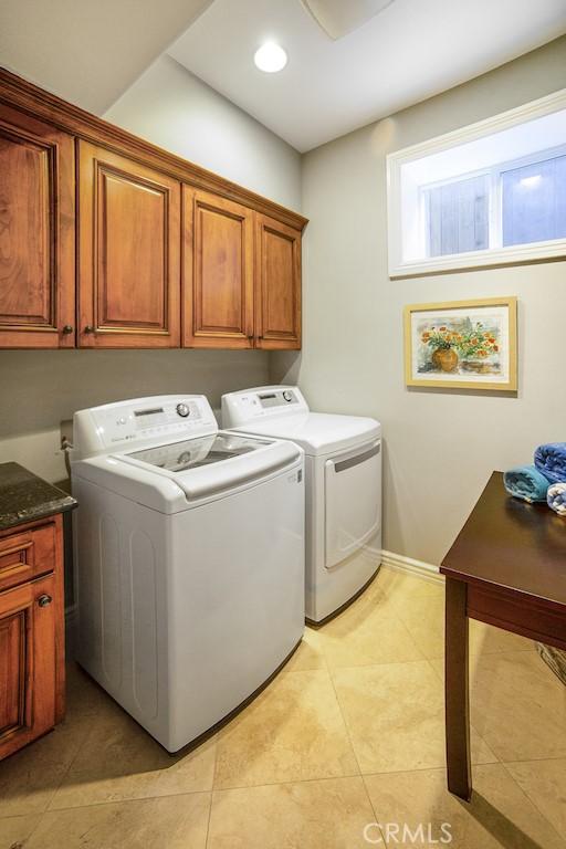 clothes washing area featuring cabinet space, light tile patterned floors, and washing machine and clothes dryer