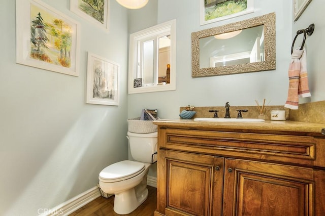 half bathroom featuring baseboards, vanity, toilet, and wood finished floors