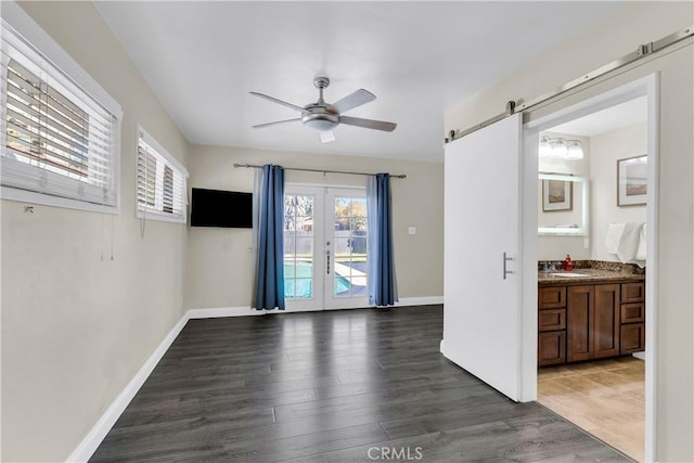 spare room featuring dark wood-type flooring, french doors, sink, ceiling fan, and a barn door