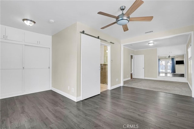 unfurnished room featuring ceiling fan, a barn door, and dark hardwood / wood-style floors