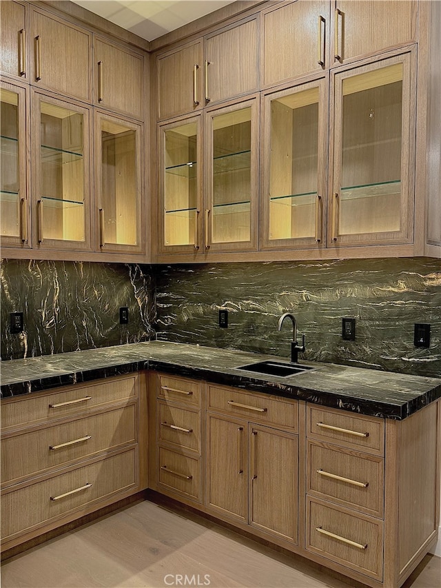 kitchen featuring backsplash, dark stone counters, sink, and light hardwood / wood-style flooring