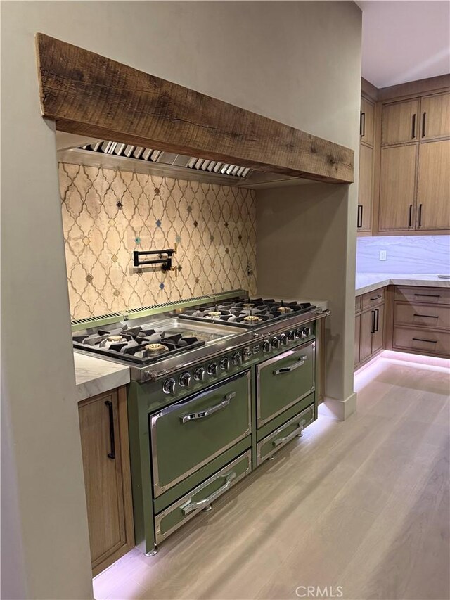 kitchen with custom exhaust hood, double oven range, backsplash, and light hardwood / wood-style floors