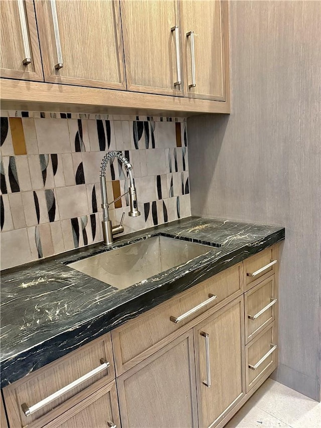 kitchen with a sink, light tile patterned floors, dark stone counters, and backsplash