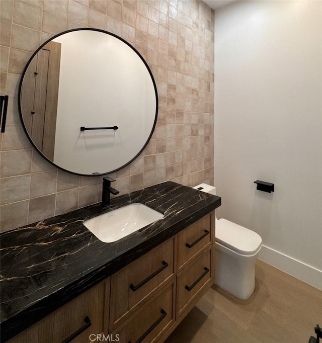 half bath featuring toilet, vanity, baseboards, tile walls, and tasteful backsplash