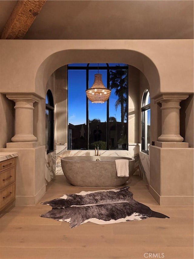 bathroom with a freestanding tub, wood finished floors, and ornate columns