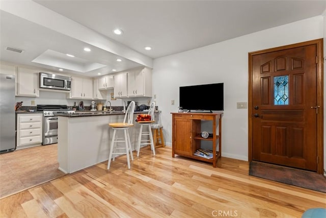 kitchen with white cabinets, stainless steel appliances, light hardwood / wood-style floors, kitchen peninsula, and a breakfast bar area