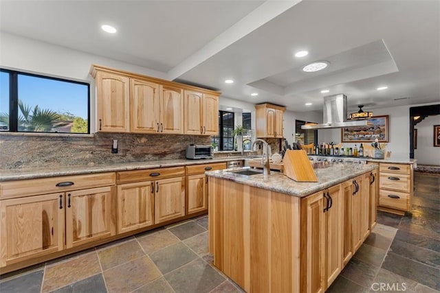 kitchen featuring island range hood, a center island with sink, light brown cabinets, a tray ceiling, and sink