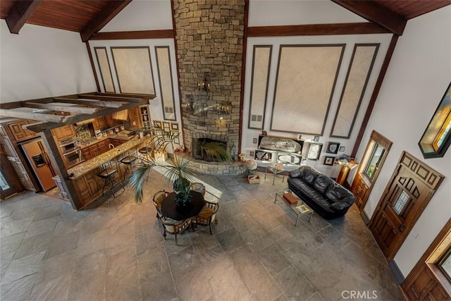 living room with high vaulted ceiling, beamed ceiling, a stone fireplace, and wooden ceiling