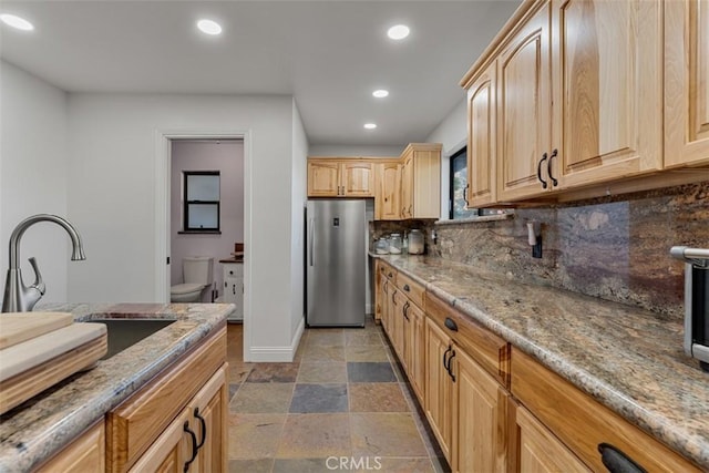 kitchen with tasteful backsplash, light brown cabinets, stainless steel refrigerator, light stone counters, and sink