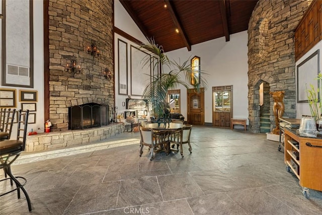 unfurnished dining area featuring high vaulted ceiling, beam ceiling, a stone fireplace, and wooden ceiling