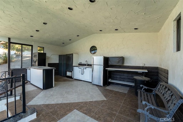 kitchen featuring dark tile patterned floors, a center island, lofted ceiling, sink, and stainless steel fridge