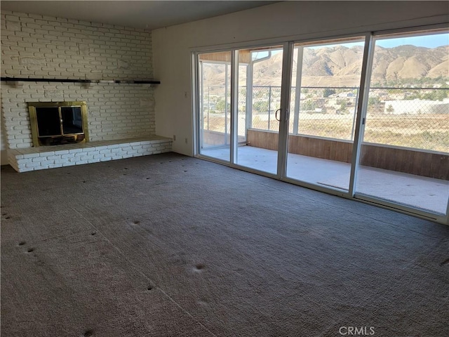 unfurnished living room with a mountain view, carpet floors, and a brick fireplace