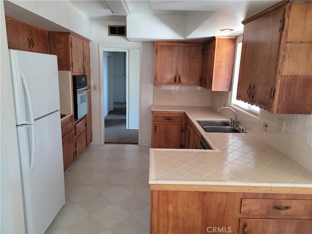 kitchen featuring tile counters, white refrigerator, sink, wall oven, and kitchen peninsula