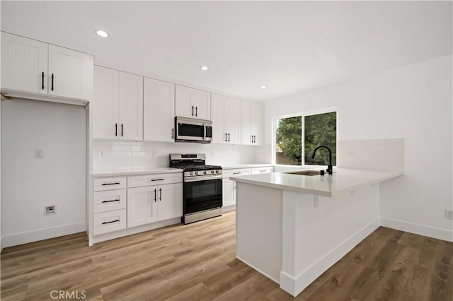 kitchen featuring light hardwood / wood-style floors, kitchen peninsula, sink, white cabinetry, and stainless steel appliances