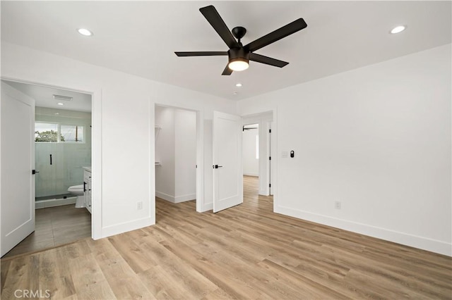 unfurnished bedroom with a spacious closet, connected bathroom, a closet, light wood-type flooring, and ceiling fan