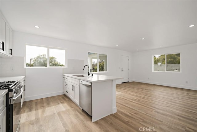 kitchen with light hardwood / wood-style floors, kitchen peninsula, appliances with stainless steel finishes, white cabinets, and sink