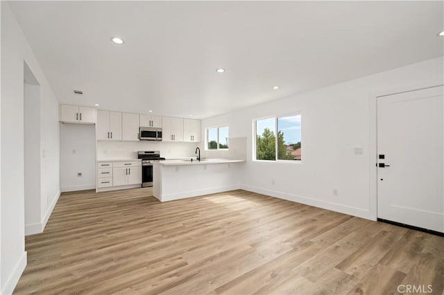 kitchen featuring light hardwood / wood-style floors, kitchen peninsula, white cabinetry, appliances with stainless steel finishes, and a breakfast bar area