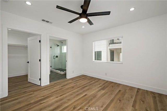 unfurnished bedroom with ceiling fan, ensuite bathroom, hardwood / wood-style floors, a spacious closet, and a closet