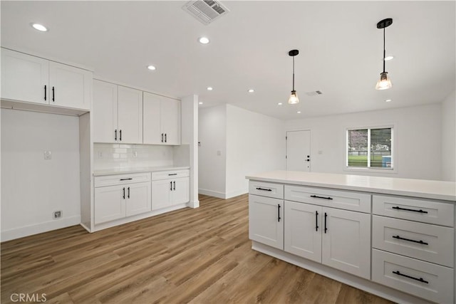 kitchen with white cabinets, decorative backsplash, light hardwood / wood-style floors, and pendant lighting