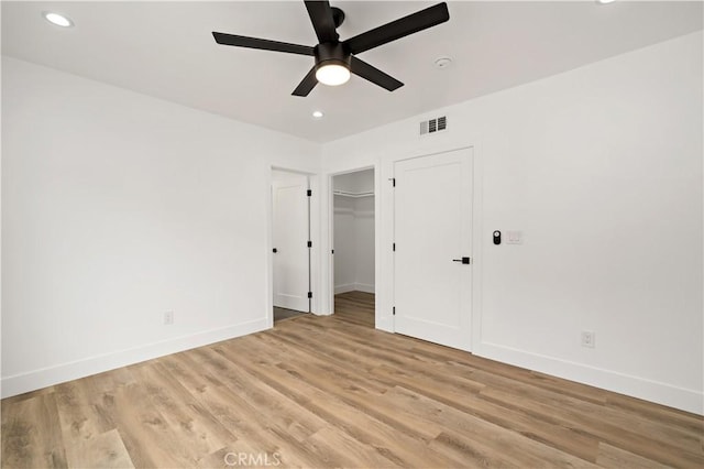 unfurnished bedroom featuring a spacious closet, ceiling fan, a closet, and light hardwood / wood-style flooring