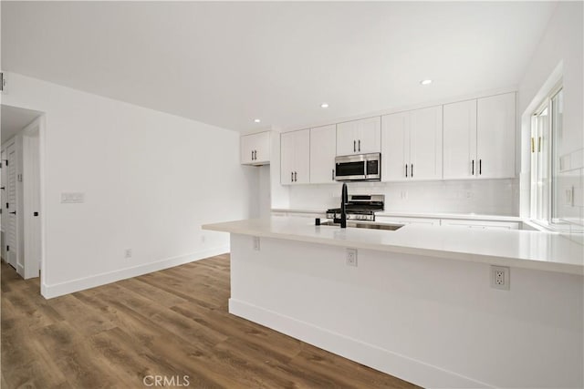 kitchen with kitchen peninsula, stainless steel appliances, white cabinets, light hardwood / wood-style flooring, and sink