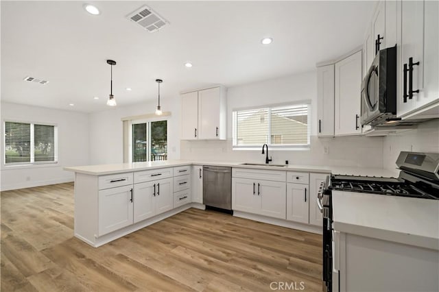 kitchen featuring white cabinetry, stainless steel appliances, sink, hanging light fixtures, and kitchen peninsula