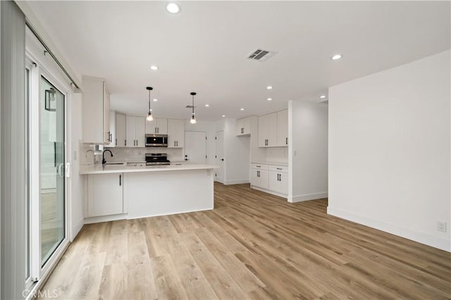 kitchen with light hardwood / wood-style floors, pendant lighting, kitchen peninsula, white cabinetry, and stainless steel appliances