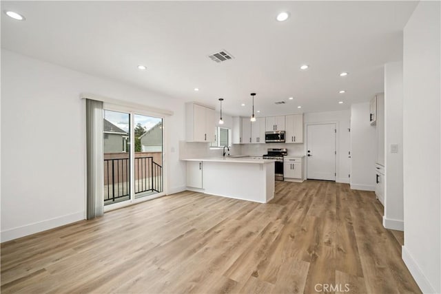 kitchen featuring pendant lighting, kitchen peninsula, white cabinetry, light hardwood / wood-style flooring, and stainless steel appliances