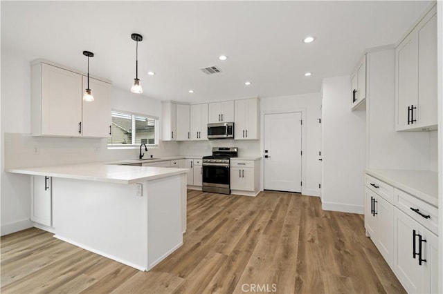 kitchen featuring pendant lighting, kitchen peninsula, sink, stainless steel appliances, and white cabinets