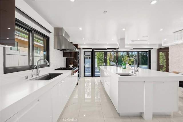 kitchen featuring a large island, sink, white cabinets, and wall chimney exhaust hood