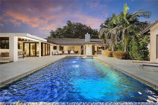 pool at dusk with pool water feature and a patio