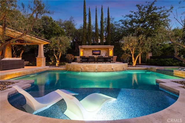 pool at dusk with pool water feature, a water slide, outdoor lounge area, a bar, and a patio