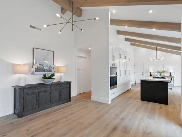 interior space featuring decorative light fixtures, light wood-type flooring, a notable chandelier, a kitchen island, and beam ceiling