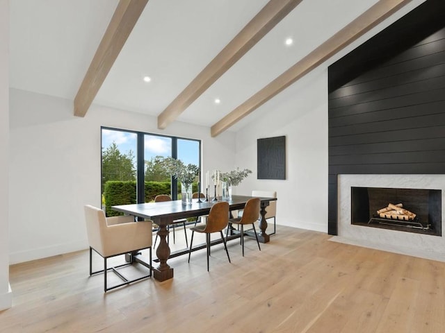 dining room with light hardwood / wood-style flooring, a fireplace, and vaulted ceiling with beams