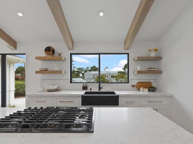 kitchen featuring black gas cooktop, sink, beamed ceiling, white cabinetry, and light stone countertops