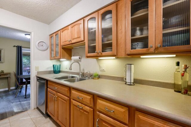 kitchen featuring a textured ceiling, light tile patterned floors, stainless steel dishwasher, and sink