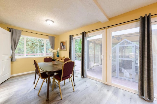 dining room featuring a textured ceiling, light hardwood / wood-style flooring, and beamed ceiling