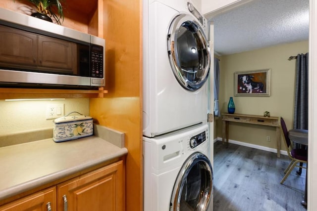 laundry room with stacked washing maching and dryer, dark wood-type flooring, a textured ceiling, and cabinets