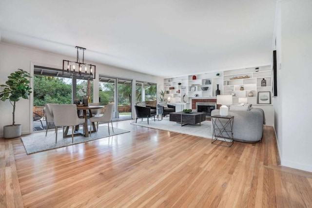 living room with an inviting chandelier, a brick fireplace, built in shelves, and light wood-type flooring