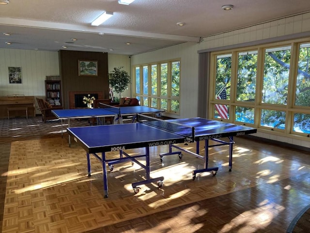 recreation room with parquet floors, wooden walls, beam ceiling, and a textured ceiling