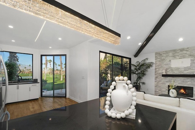 unfurnished living room featuring sink, beam ceiling, a stone fireplace, and dark hardwood / wood-style floors