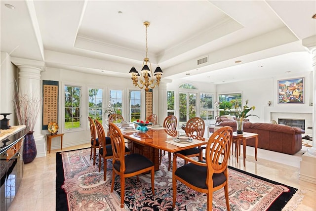 dining space featuring a raised ceiling, a chandelier, and ornate columns