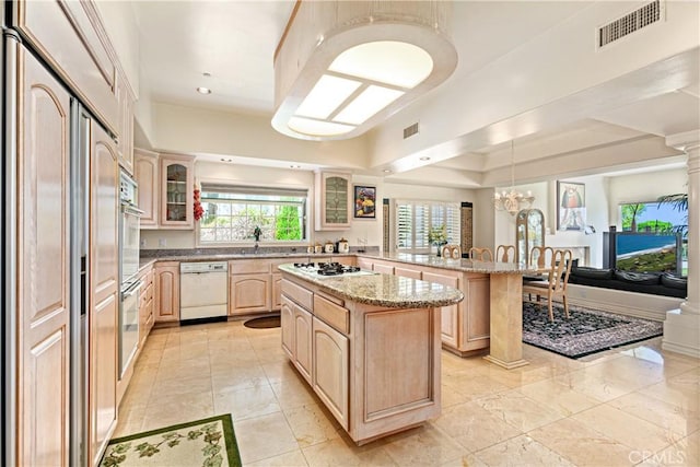 kitchen with a notable chandelier, a center island, white appliances, light brown cabinets, and decorative columns