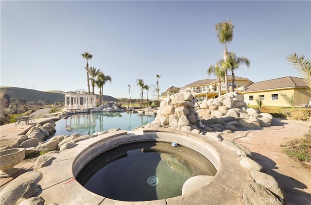 view of swimming pool featuring a water view and an in ground hot tub